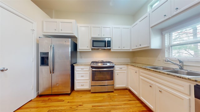 kitchen featuring stainless steel appliances, sink, light hardwood / wood-style flooring, and light stone counters