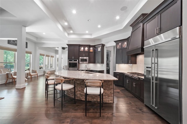 kitchen featuring custom range hood, dark brown cabinetry, stainless steel appliances, sink, and an island with sink