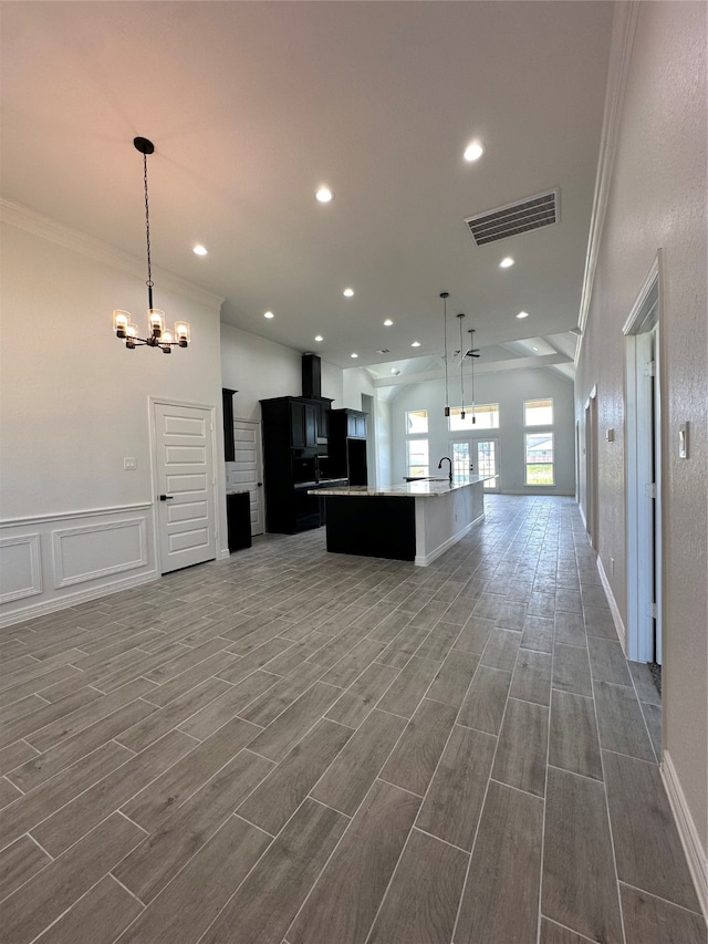 kitchen featuring decorative light fixtures, an inviting chandelier, crown molding, a kitchen island with sink, and wood-type flooring