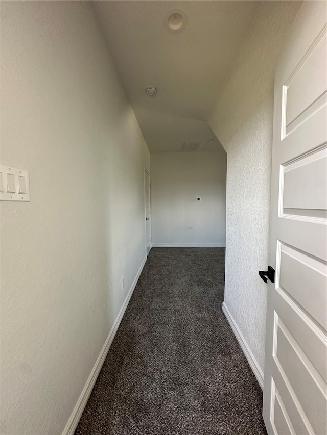 hall with dark carpet and lofted ceiling