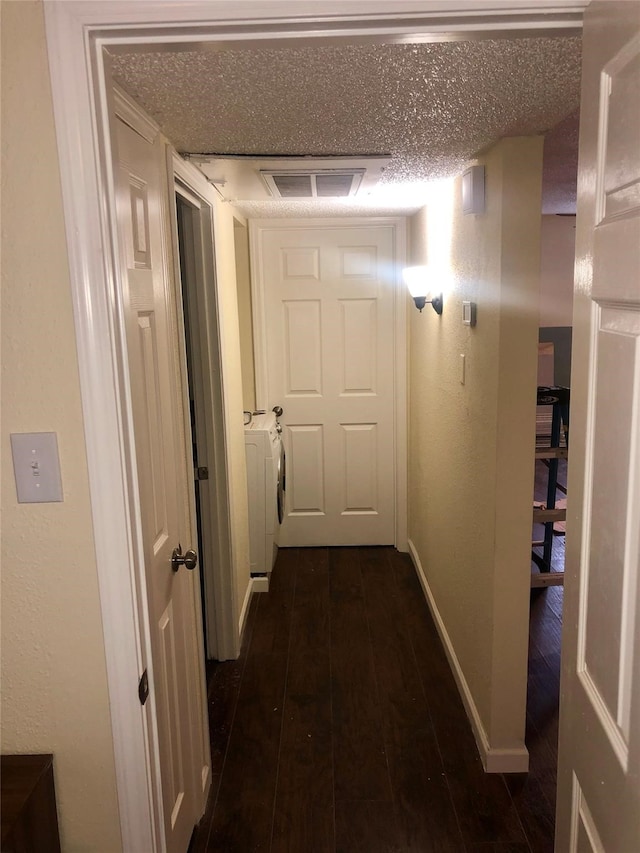 hallway with a textured ceiling, washer and clothes dryer, and dark hardwood / wood-style flooring