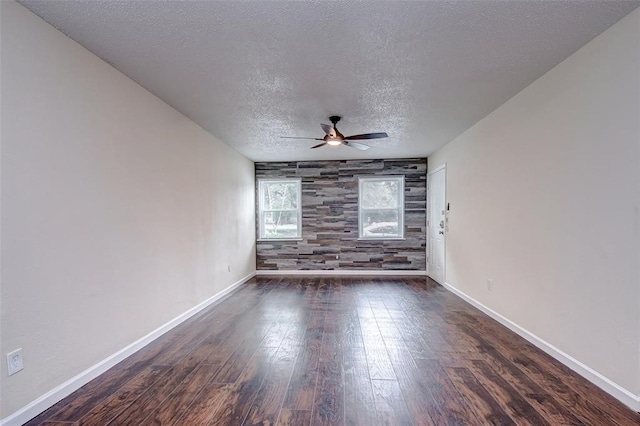 spare room featuring dark wood-type flooring, wood walls, ceiling fan, and a textured ceiling