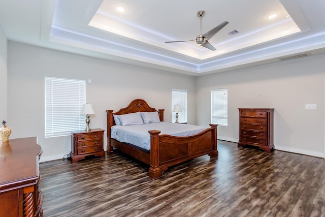 bedroom with dark hardwood / wood-style floors, ceiling fan, and a tray ceiling