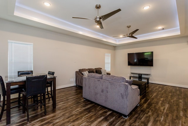 living room featuring a raised ceiling, ceiling fan, and dark wood-type flooring