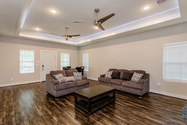 living room with ceiling fan, a tray ceiling, and dark hardwood / wood-style flooring