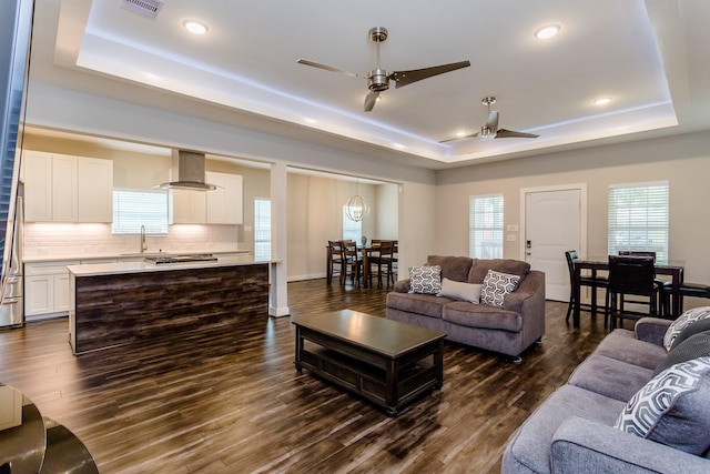 living room with ceiling fan, sink, a tray ceiling, and dark hardwood / wood-style floors