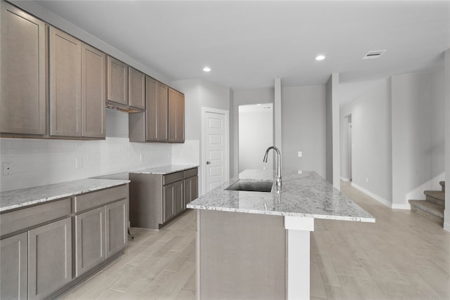 kitchen featuring tasteful backsplash, a center island with sink, light stone countertops, sink, and light hardwood / wood-style flooring