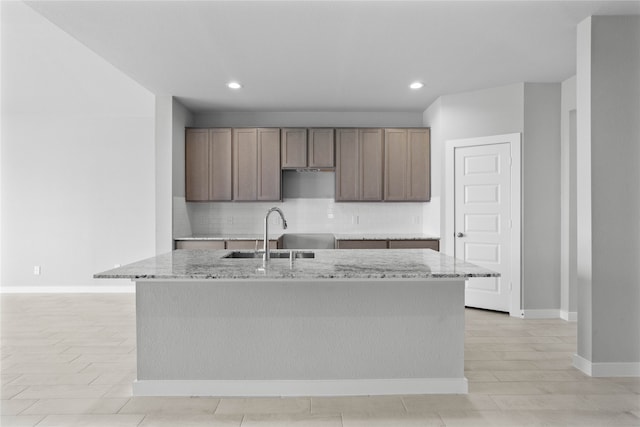 kitchen with a kitchen island with sink, decorative backsplash, sink, and light stone counters