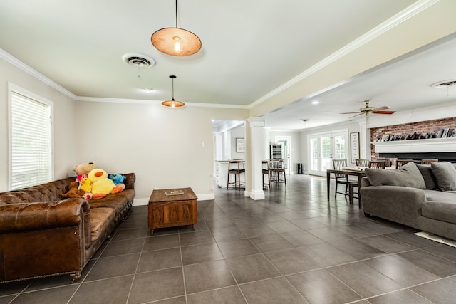 tiled living room featuring ornate columns, ceiling fan, a fireplace, and crown molding