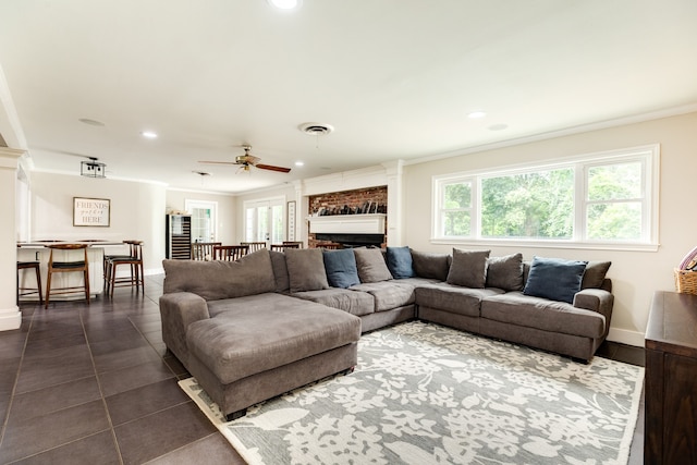 living room featuring dark tile floors, ceiling fan, a fireplace, and crown molding