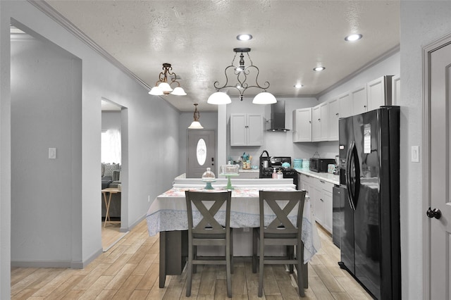 kitchen with a kitchen island with sink, wall chimney range hood, a textured ceiling, pendant lighting, and black appliances