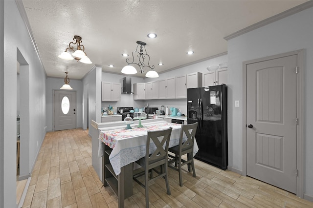 kitchen featuring white cabinets, wall chimney exhaust hood, pendant lighting, and black fridge