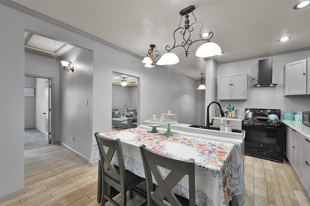 kitchen featuring a center island with sink, black gas range oven, pendant lighting, wall chimney range hood, and crown molding