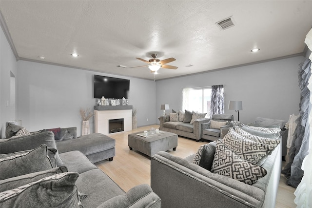 living room with ceiling fan, light wood-type flooring, ornamental molding, and a textured ceiling