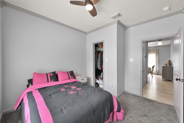 bedroom with a spacious closet, ceiling fan, carpet, a closet, and crown molding