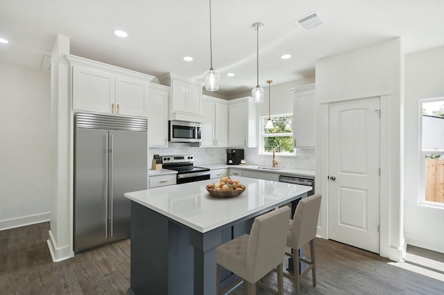 kitchen with dark wood-type flooring, white cabinets, pendant lighting, a kitchen island, and appliances with stainless steel finishes