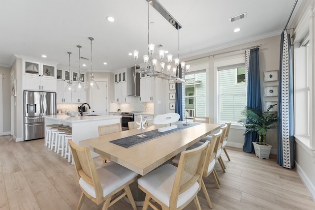 dining room featuring sink, an inviting chandelier, light hardwood / wood-style floors, and ornamental molding