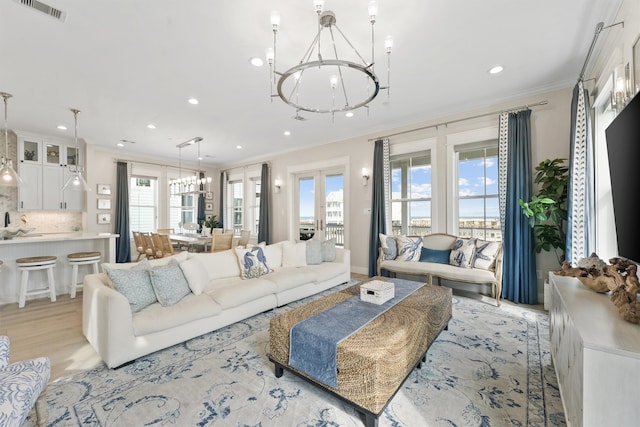 living room featuring a chandelier, light hardwood / wood-style flooring, plenty of natural light, and ornamental molding