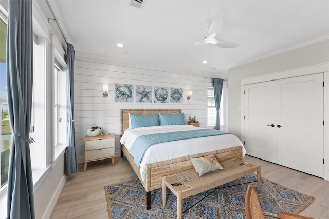 bedroom with crown molding, wooden walls, ceiling fan, light hardwood / wood-style floors, and a closet