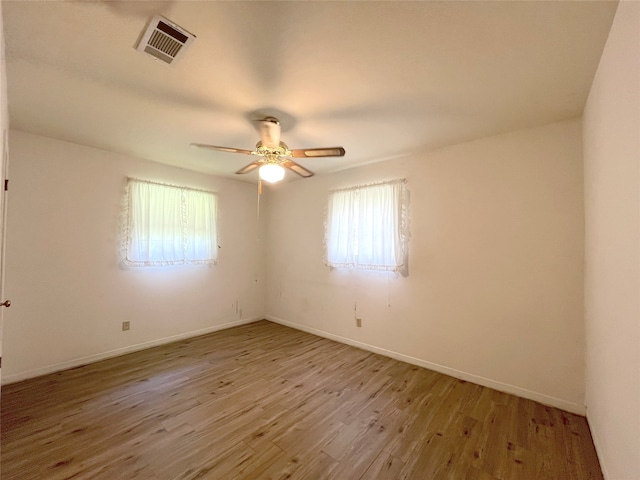 empty room with a healthy amount of sunlight, ceiling fan, and hardwood / wood-style flooring