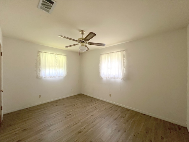 empty room with a wealth of natural light, hardwood / wood-style flooring, and ceiling fan