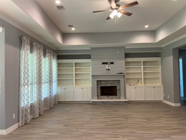 unfurnished living room featuring ceiling fan, a raised ceiling, light hardwood / wood-style flooring, and a stone fireplace