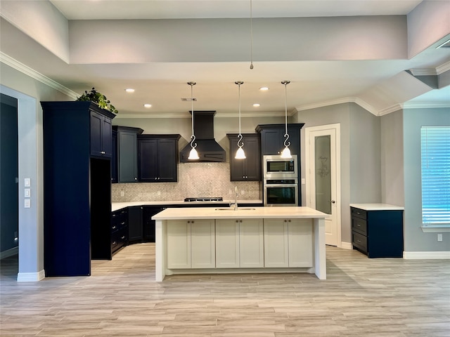 kitchen featuring backsplash, stainless steel microwave, custom range hood, an island with sink, and hanging light fixtures