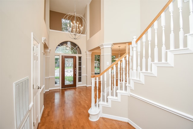 entryway with decorative columns, hardwood / wood-style flooring, a towering ceiling, and a chandelier