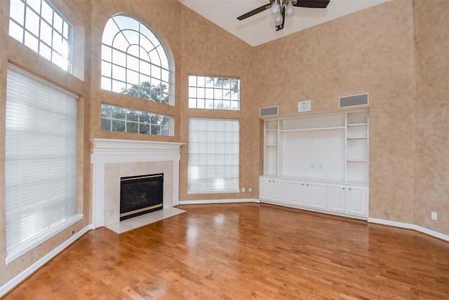 unfurnished living room featuring wood-type flooring, a high ceiling, ceiling fan, and a premium fireplace