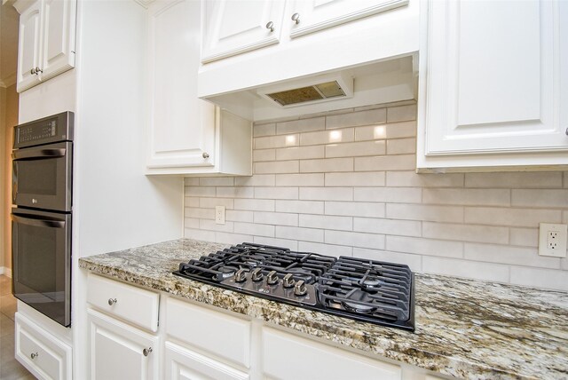 kitchen with black gas cooktop, white cabinetry, decorative backsplash, light stone countertops, and double oven