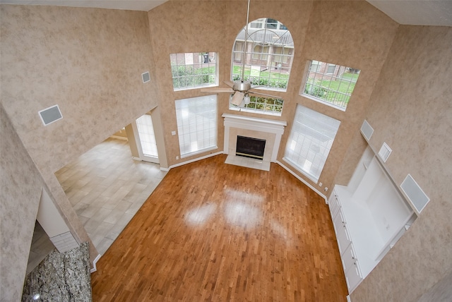 unfurnished living room with ceiling fan, light wood-type flooring, and a towering ceiling