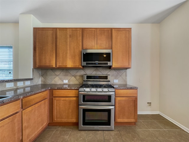 kitchen featuring tile floors, stainless steel appliances, backsplash, and dark stone countertops