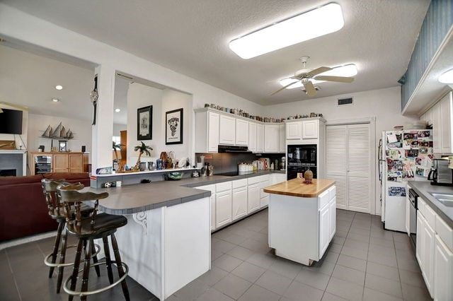 kitchen with a kitchen island, exhaust hood, ceiling fan, tile floors, and white cabinets