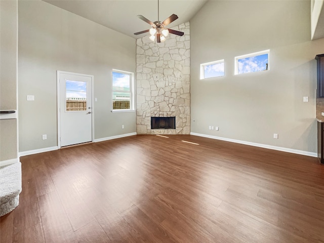 unfurnished living room with high vaulted ceiling, dark wood-type flooring, a stone fireplace, and ceiling fan