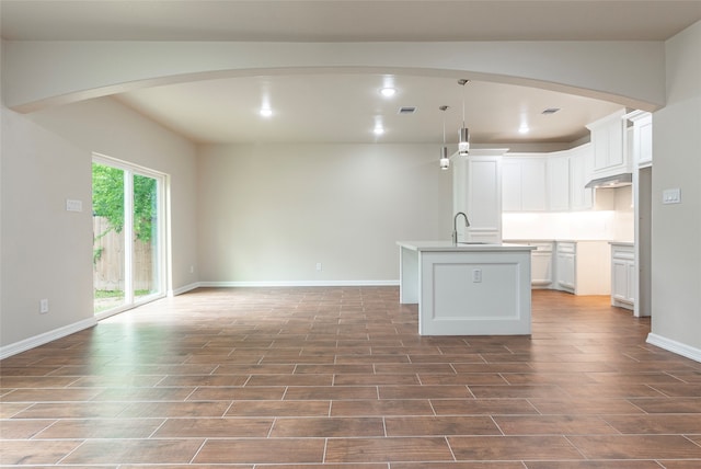 kitchen with an island with sink, white cabinetry, wall chimney exhaust hood, sink, and dark tile floors