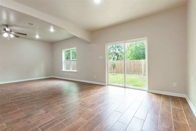 empty room featuring a healthy amount of sunlight, wood-type flooring, beam ceiling, and ceiling fan