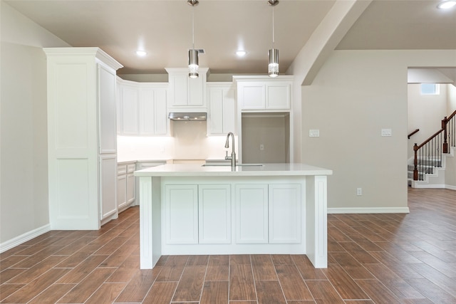 kitchen with white cabinetry, a kitchen island with sink, decorative light fixtures, wood-type flooring, and sink