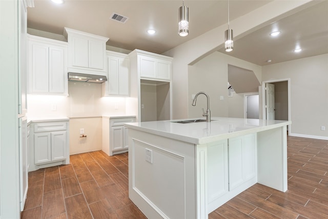 kitchen featuring decorative light fixtures, dark wood-type flooring, sink, a kitchen island with sink, and white cabinetry