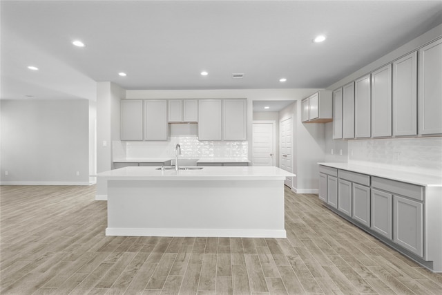 kitchen with gray cabinetry, light wood-type flooring, sink, and an island with sink