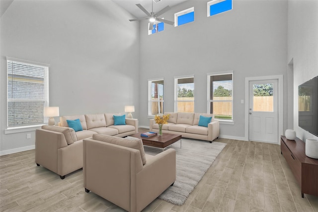 living room featuring a towering ceiling, light wood-type flooring, and ceiling fan