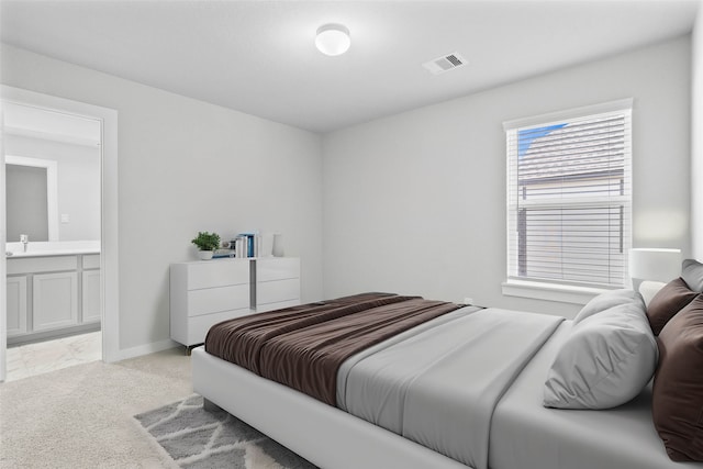 bedroom with ensuite bathroom and light colored carpet