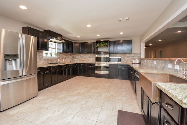 kitchen featuring stainless steel appliances, dark brown cabinetry, light stone counters, backsplash, and light tile floors