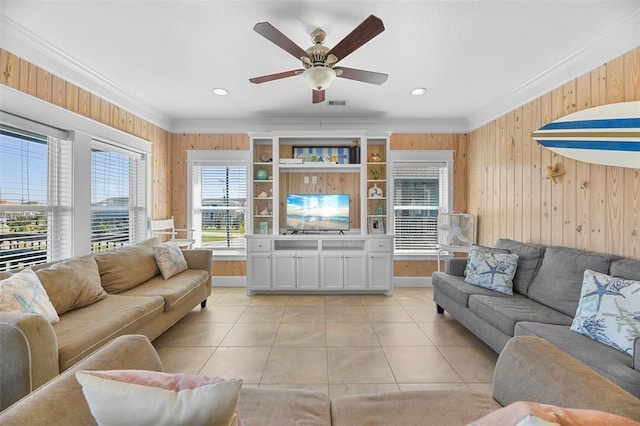 living room featuring wooden walls, ceiling fan, ornamental molding, and light tile floors