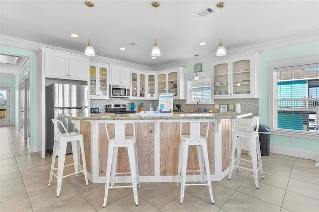 kitchen with appliances with stainless steel finishes, white cabinets, tasteful backsplash, and a breakfast bar