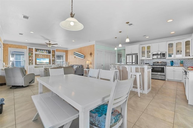 tiled dining space with ceiling fan and ornamental molding