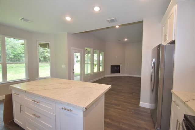 kitchen featuring stainless steel refrigerator, white cabinetry, a center island, light stone countertops, and dark wood-type flooring