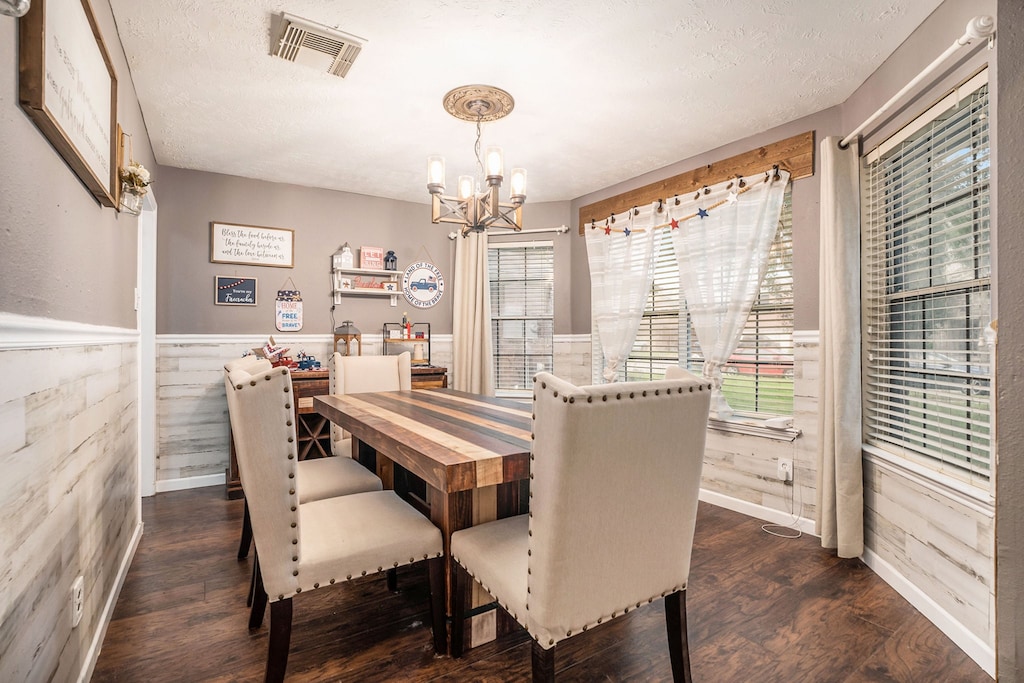 dining area with a textured ceiling, dark wood-type flooring, wooden walls, and an inviting chandelier