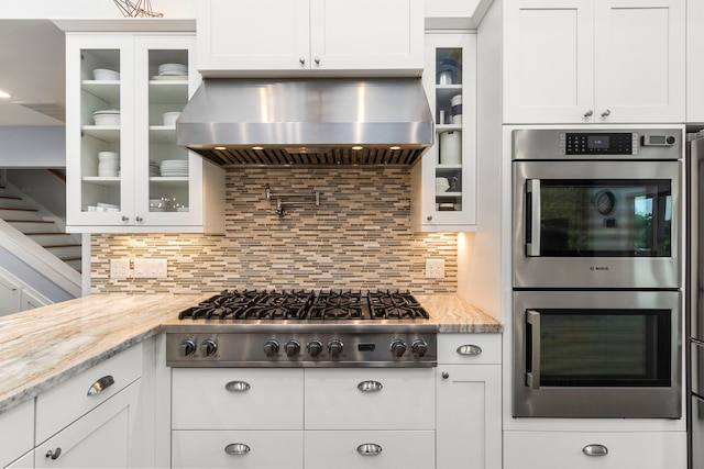 kitchen with appliances with stainless steel finishes, tasteful backsplash, white cabinetry, and wall chimney range hood