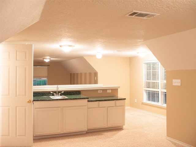 kitchen featuring light carpet, a textured ceiling, sink, white cabinetry, and lofted ceiling