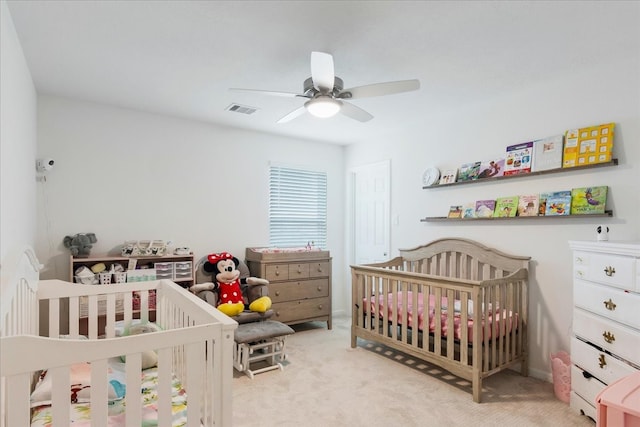 bedroom featuring light colored carpet, ceiling fan, and a crib